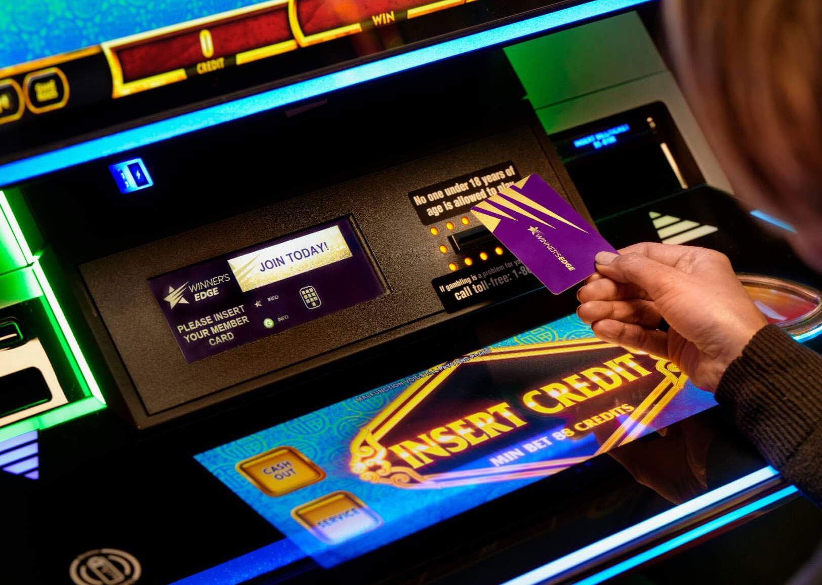 A member hand holding the Winner’s Edge card by a slot machine